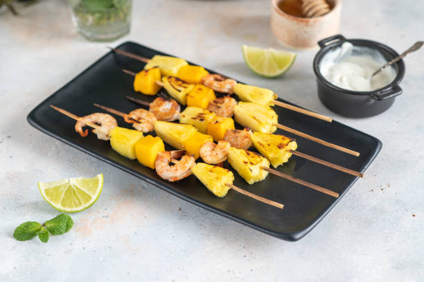 istock Grilled shrimp skewers with pineapple and mango. Shrimp skewers with mint, pineapple, mango, lime and yogurt sauce on a black plate. 1394281946