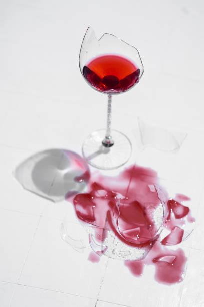 istock Broken glass with red wine on a table with white tiles 1394281977
