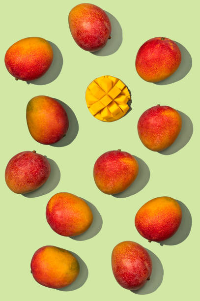 istock Mango design concept. Top view of whole and diced fresh mango fruits pattern on green background. 1394281982
