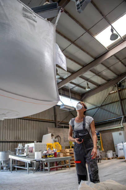 istock Blue collar woman using a hand-operated crane inside a quartz ore warehouse 1394283151