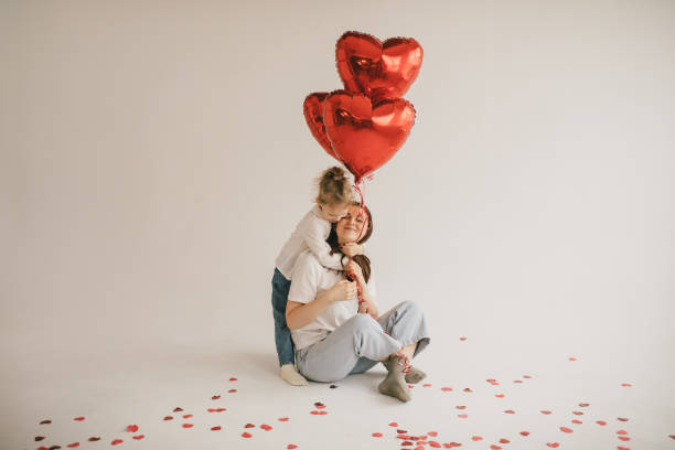 young mother and daughter holding red heart shaped balloons on white background. saint valentine's day celebration. - heart shape confetti small red imagens e fotografias de stock