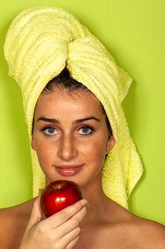 close up of a young woman with towel wrapped around her hair holding a red apple in her hand ready to eat