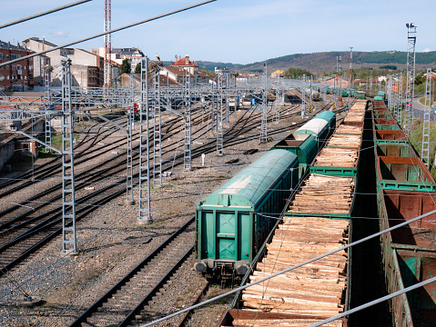 Freight wagons full of wood and other empty ones standing in rows on the parking tracks of the Monforte de Lemos station next to the catenary poles waiting for their use