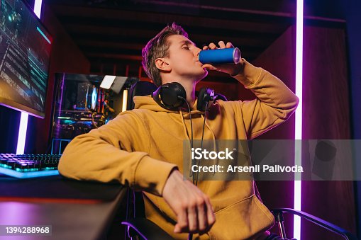 istock Yong caucasian pro gamer drinking energy drink while playing computer video games 1394288968