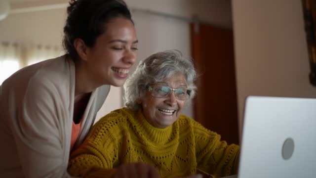 Grandmother and granddaughter using laptop and celebrating good news at home