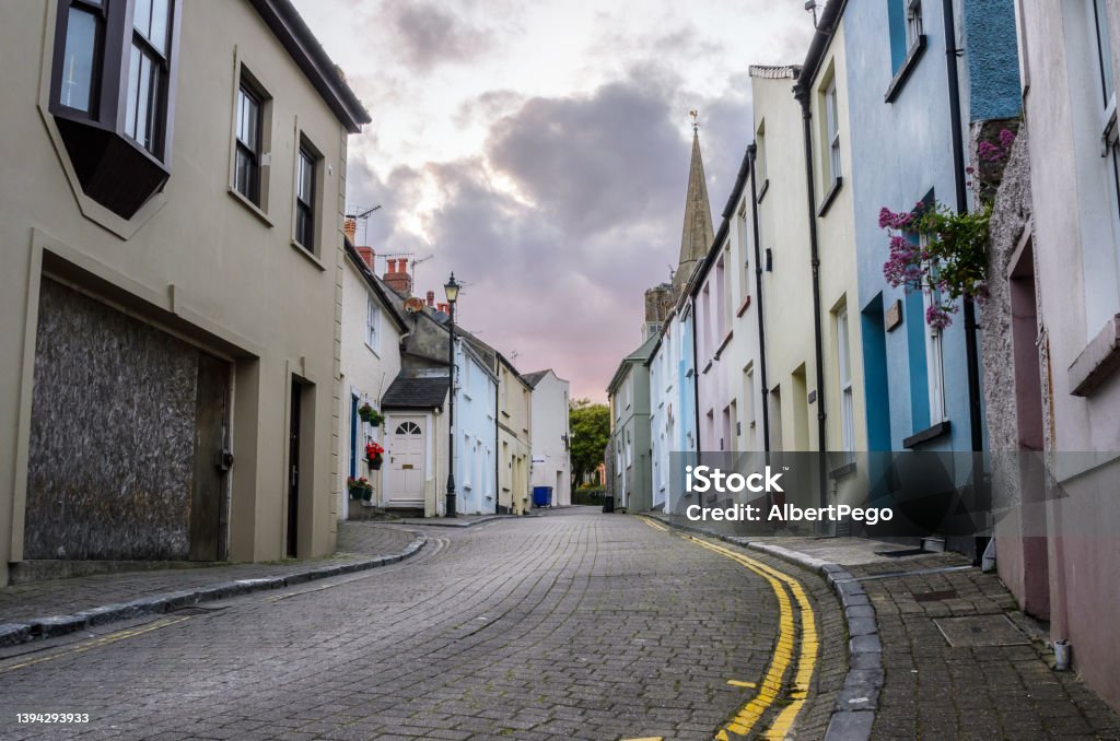 Old pastel houses along a cobblestone street in a town centre at dusk Deserted cobblestone street lined with traditional pastel row houses at dusk. Tenby, Wales, UK. UK Stock Photo