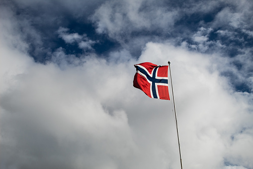 Norwegian flag flying in front of cloudy blue sky