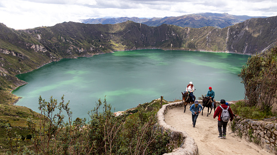 Quilotoa, Ecuador - April 16, 2022: Lake Quilotoa in caldera of eponymous volcano. Hiking footpatch and tourists riding horses to up the hill. Cotopaxi province, Ecuador