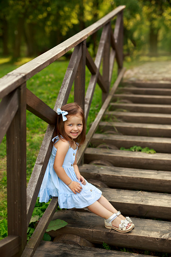 A funny amusing Girl in a bare dress is sitting on a wooden staircase in front of the house laughing merrily. A warm summer day in nature on vacation