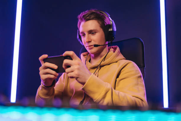 Pro cyber sportsman playing in mobile video game at home Portrait of caucasian man pro gamer sitting on gaming chair, wearing headset, has live stream while playing mobile game on the smartphone at home. Young cyber sportsman holding cellphone in hands gaming chair photos stock pictures, royalty-free photos & images