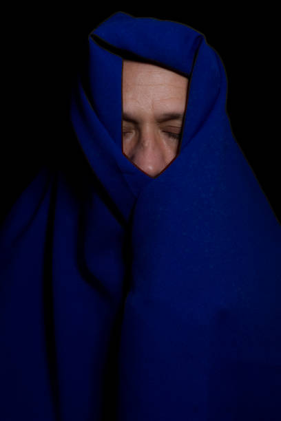 istock Man covered with blue cloth against a black background. 1394309023