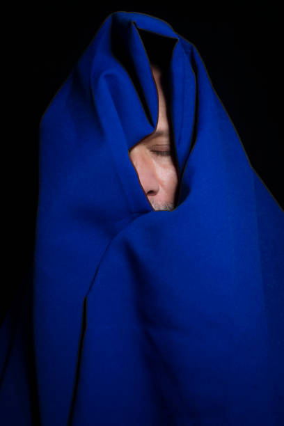 istock Man covered with blue cloth against a black background. 1394309028