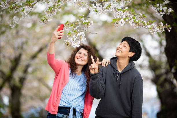 A mother with her mixed race son in a public park with Japanese cherry blossoms taking a selfie.