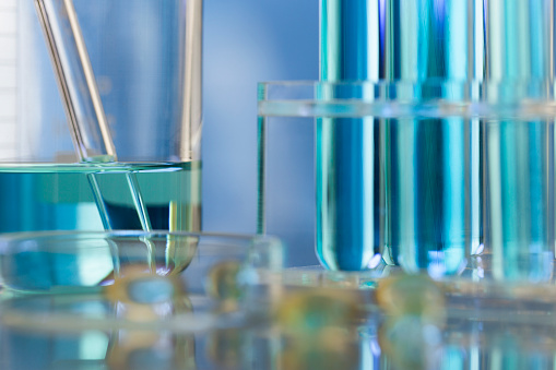 Neatly arranged test tubes containing blue reagent in chemistry laboratory with beaker and soft capsule - stock photo