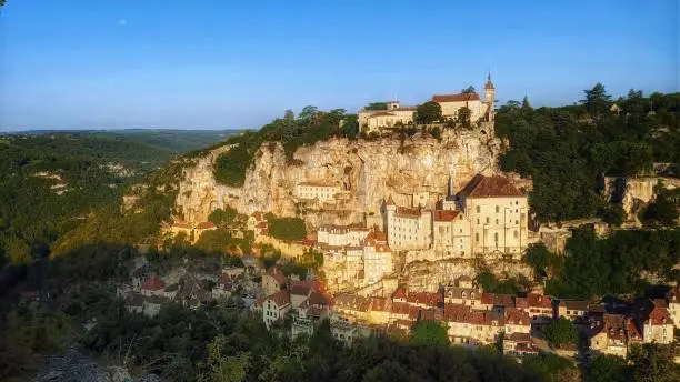 Sunrise over the medieval village of Rocamadour, a holy complex of monastic buildings and pilgrimage churches, perched on the side of a limestone cliff over the Alzou canyon. Lot, France.