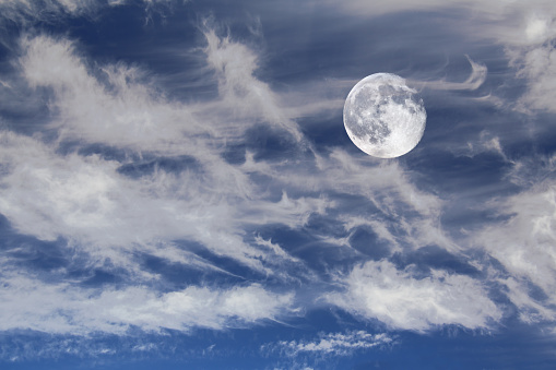 Waning moon on blue sky with cirrus clouds.