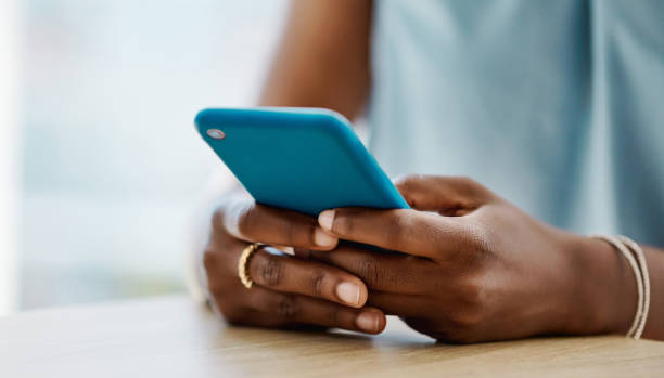 afrikanische frau, die allein in einem büro ein handy benutzt - sms stock-fotos und bilder