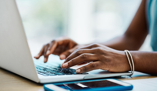 Black woman typing and browsing on a laptop in an office alone