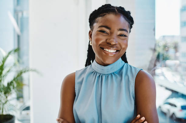 giovane imprenditrice nera sicura di sé in piedi a una finestra in un ufficio da sola - sorridere foto e immagini stock