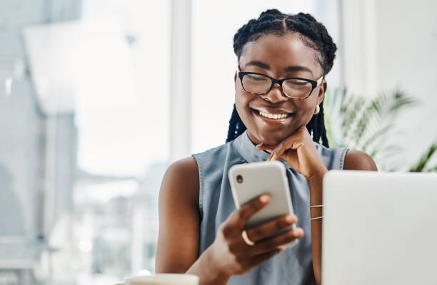 istock Happy young black businesswoman using a cellphone while working on a laptop in an office alone 1394347617