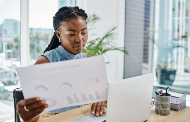 istock Young african businesswoman looking at graphs while working on a laptop in an office alone 1394347629