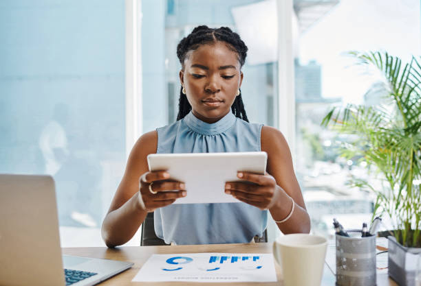 istock Focused young black businesswoman using a digital tablet while analysing graphs in an office alone 1394347631