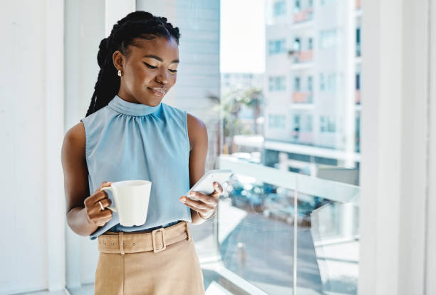 istock Black businesswoman drinking coffee while texting on a cellphone at a window in an office alone 1394347644