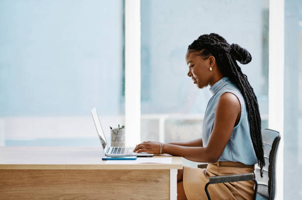 Young black businesswoman working on a laptop in an office alone Young black businesswoman working on a laptop in an office alone using laptop stock pictures, royalty-free photos & images