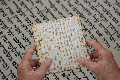 Passover  Hands holding matzo on Hebrew script background
