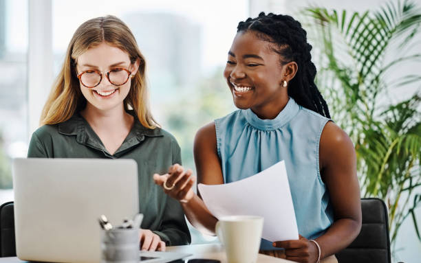 istock Two cheerful businesswomen going through paperwork while using a laptop together in an office 1394348670