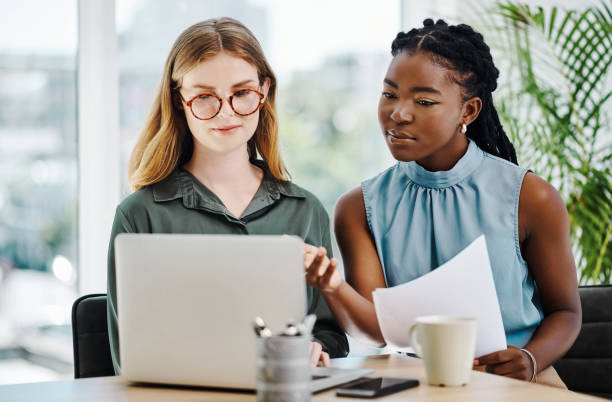 istock Two focused young businesswomen working together on a laptop while going through paperwork in an office 1394348674