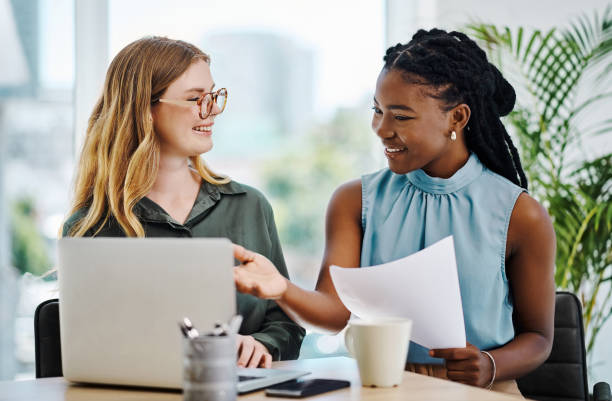 istock Two smiling businesswomen going through paperwork while using a laptop together in an office 1394348678
