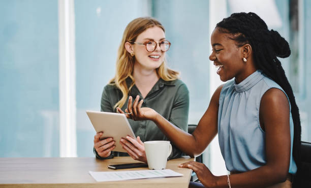 Two confident young businesswomen working together on a digital tablet in an office stock photo
