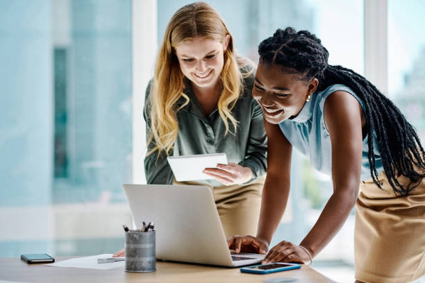 Two diverse businesswomen working together on a digital tablet and laptop in an office stock photo