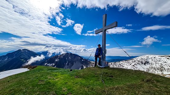 Hiker man at the summit cross of Rosenkogel (Rozca) with scenic view on mountain peaks in the Karawanks, Carinthia, Austria. Border with Slovenia. Triglav National Park. Alps in spring. Goal