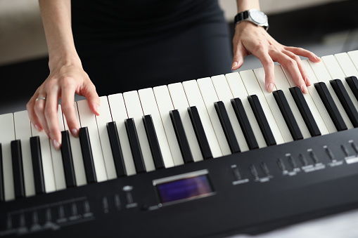 Top view of female playing on electrical piano instrument. Black and white key. Different buttons on display. Young woman exercise at home. Spare time and hobby concept