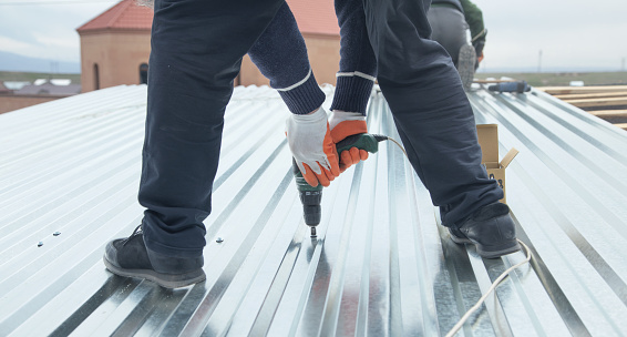 Man installing metal sheet roof by electrical drilling machine.