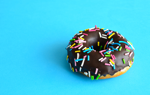 chocolate donut with coloured sprinkles isolated on blue background