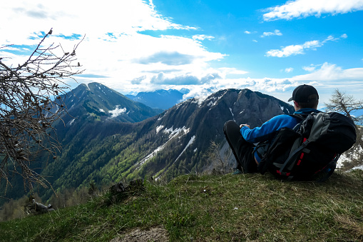 Male hiker having a break in spring on the summit of Frauenkogel in the Karawanks in Carinthia, Austria, Europe. Borders with Slovenia. Triglav National Park. Looking on Kahlkogel and Hahnkogel.