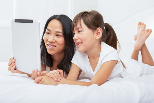 Smiling multiracial family using digital tablet laying in bedroom