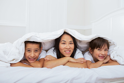 Smiling multiracial family laying under duvet in bed.