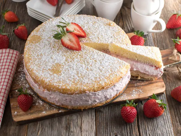 Homemade fresh baked strawberry cream cake with viennese cake base. Served on rustic and wooden table background with cross section view.