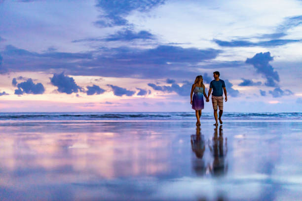 Happy couple talking while holding hands and walking on the beach at dusk. Copy space.
