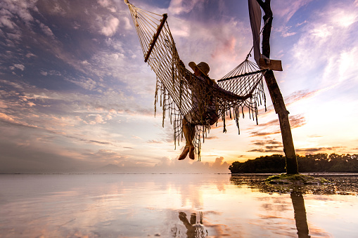 Low angle view of carefree woman relaxing in hammock above the sea. Copy space.