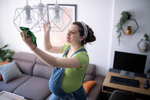 Young pregnant woman cleaning off the dust from chandelier.