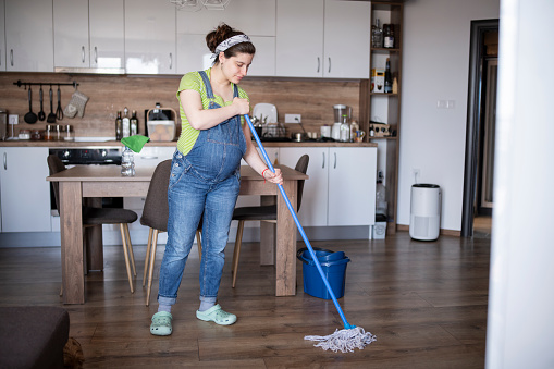 Active pregnant woman mopping the floor at home.