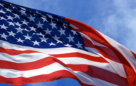 Close-up of American flag waving against blue sky.