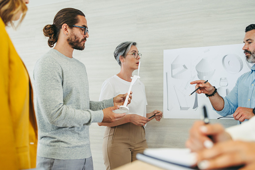 Team of creative designers having a discussion while working with wind turbine 3D models and drawings. Group of innovative businesspeople planning a renewable energy project.