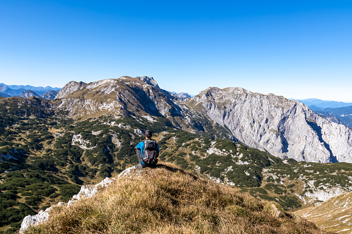 A man with a backpack enjoying panoramic view on the mountain peaks of the Hochschwab Region in Upper Styria, Austria. Sharp summits of Ebenstein and Hinterer Polster, Alps in Europe. Concept freedom