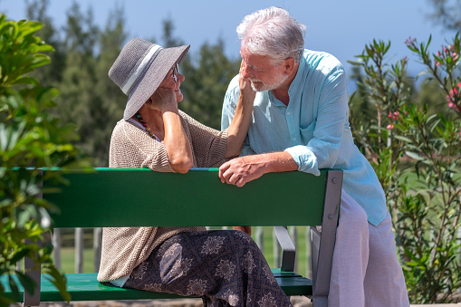 Two elderly women sitting on bench in park smiling happy life long friends enjoying retirement